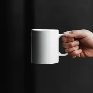 A person holding a white ceramic coffee mug by the handle wi