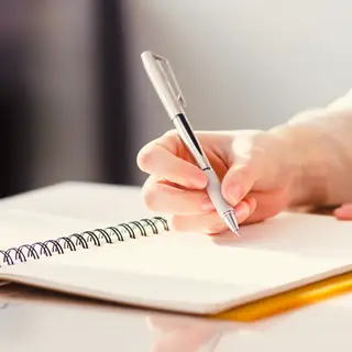 A woman writing in a notebook with a pen gripped correctly i