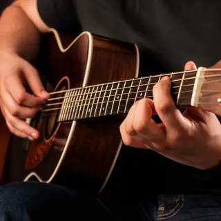 A person playing an acoustic guitar with left hand on the fr