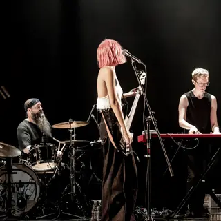 Three musicians on stage: a tall woman with short pink hair 