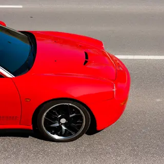 A bright red sports car parked on a gray asphalt road — the 