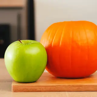 A green apple and an orange pumpkin on a wooden cutting boar