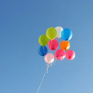 Exactly 11 colorful balloons floating against a clear blue s