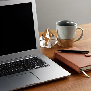 A workspace desk with a brushed aluminum laptop, a leather-b