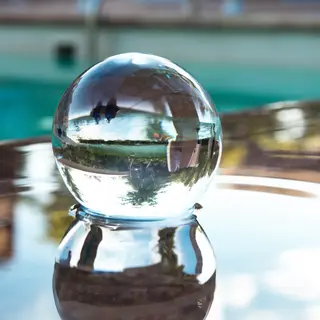 A clear glass sphere sitting on a mirror surface near a pool