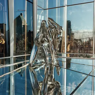 A chrome sculpture in a room with a glass floor and large wi