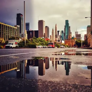 A city skyline reflected in a rain puddle on a street, with 