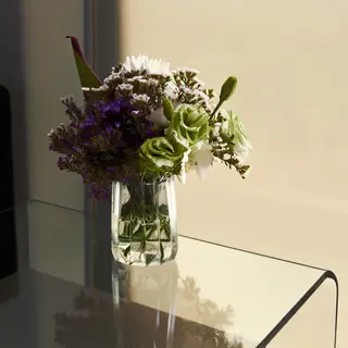 A vase of flowers on a glass table with a clear reflection v