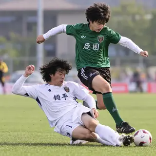 Two soccer players mid-tackle, one sliding and the other jum