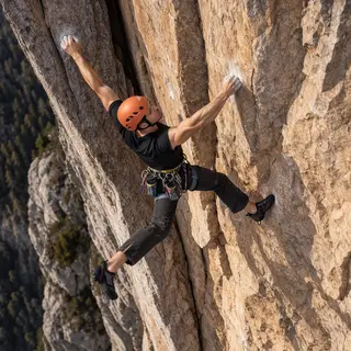 A rock climber clinging to a cliff face with arms and legs e