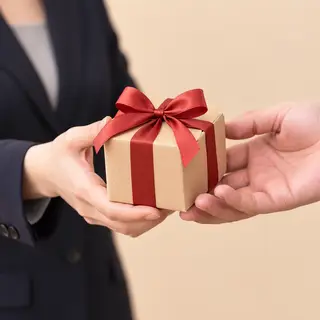 One person handing a small gift box to another person, both 