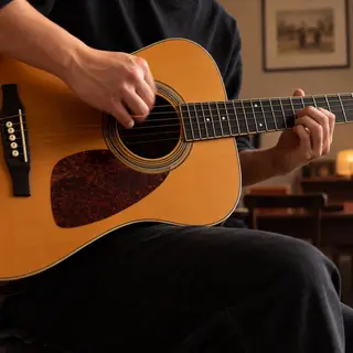 A person playing an acoustic guitar with left hand on the fr