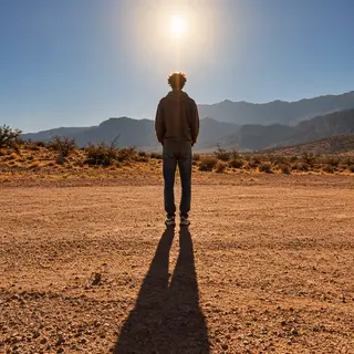 A person standing outdoors at midday with a short shadow dir