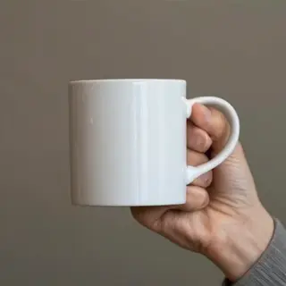 A person holding a white ceramic coffee mug by the handle wi
