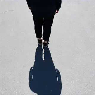 A person standing outdoors at midday with a short shadow dir