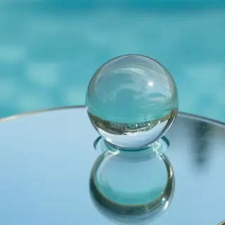 A clear glass sphere sitting on a mirror surface near a pool