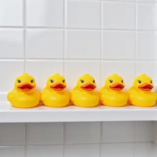 Exactly 5 yellow rubber ducks sitting in a row on a bathroom