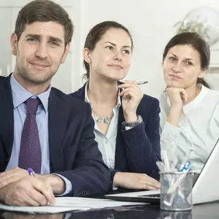 Three coworkers in a meeting: one looking frustrated with fu