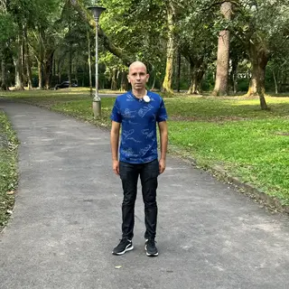A person standing in a neutral pose in a park, full body vis