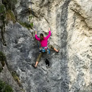 A rock climber clinging to a cliff face with arms and legs e