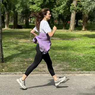 A woman mid-stride running through a park, hair and clothes 