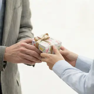 One person handing a small gift box to another person, both 