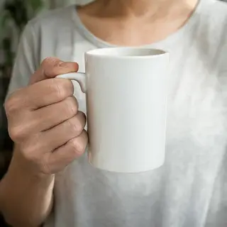 A person holding a white ceramic coffee mug by the handle wi
