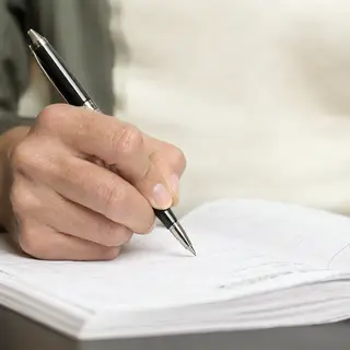 A woman writing in a notebook with a pen gripped correctly i