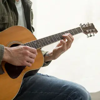 A person playing an acoustic guitar with left hand on the fr