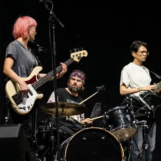 Three musicians on stage: a tall woman with short pink hair 