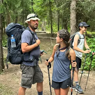 Three hikers on a trail: a man with a backpack and sunhat, a