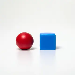 A red ball and a blue cube sitting side by side on a white s