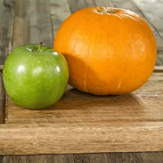 A green apple and an orange pumpkin on a wooden cutting boar