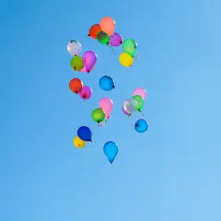 Exactly 11 colorful balloons floating against a clear blue s