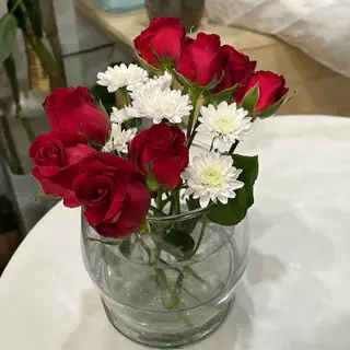 4 red roses and 2 white daisies in a glass vase on a table