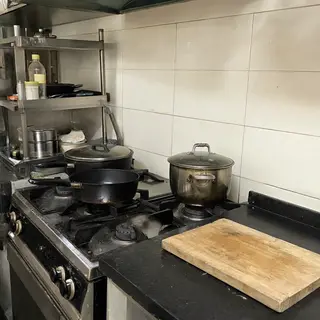 A kitchen with pots, pans, a stove, and a cutting board but 