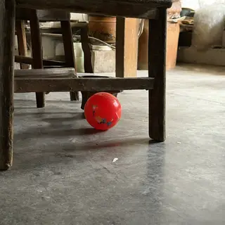 A red ball underneath a wooden chair