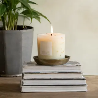 A candle on top of a stack of books, the books next to a pot