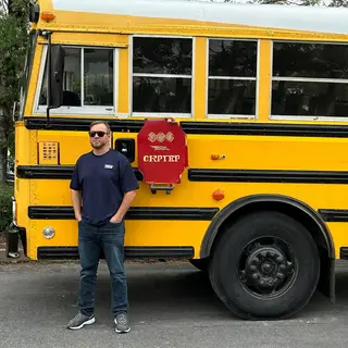 A person standing next to a yellow school bus, showing reali