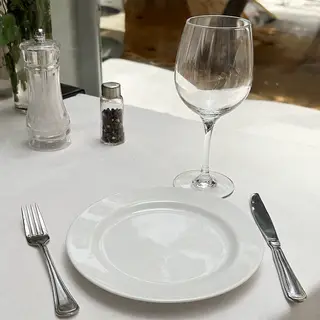 A dinner table scene with a plate, fork, knife, wine glass, 