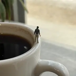 A tiny person standing on the rim of a coffee cup, looking d