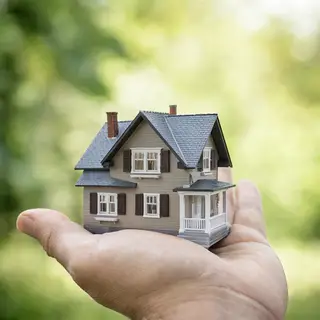 A miniature house sitting on the palm of someone's hand