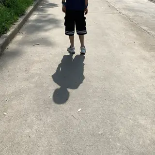 A person standing outdoors at midday with a short shadow dir