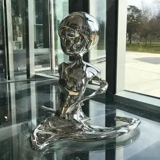 A chrome sculpture in a room with a glass floor and large wi