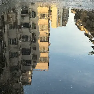 A city skyline reflected in a rain puddle on a street, with 