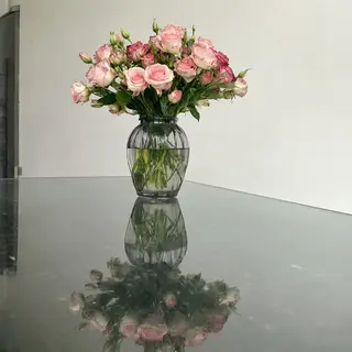 A vase of flowers on a glass table with a clear reflection v