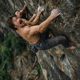 A rock climber clinging to a cliff face with arms and legs e