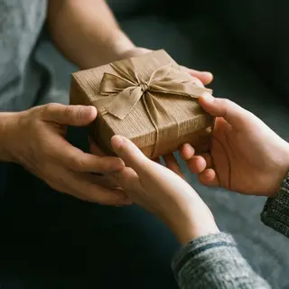 One person handing a small gift box to another person, both 