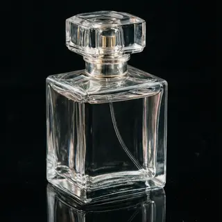 A clear glass perfume bottle on a reflective black surface w