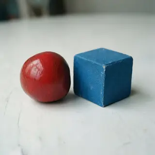 A red ball and a blue cube sitting side by side on a white s